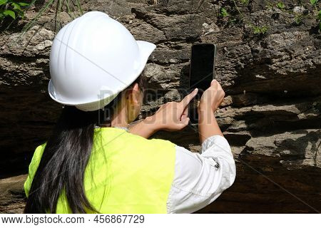 Asian Female Geologist Researcher Is Analyzing Rocks With A Smartphone In A Natural Park. Exploratio