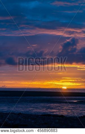 Sun Sets On Horizon Over Water Creating Beautiful Coloured Sky On New Zealand West Coast At Okarito 