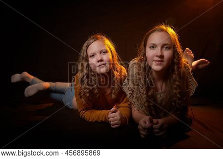 Two Cheerful Joyfull Sisters Having Fun Together In Dark Studio With Black Background