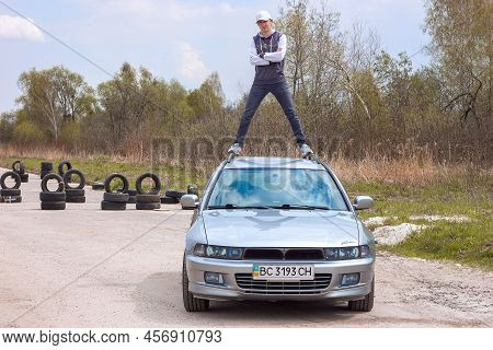 Lviv Ukraine - 05 02 2022: A Young Man In Stylish Clothes And A Cap Stands On The Roof Of A Mitsubis