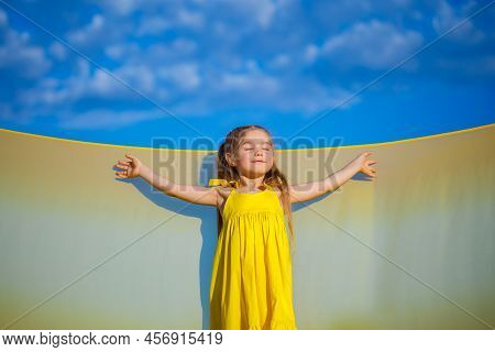 Ukrainian Girl 7 Years Old, She Is A Patriot Of Ukraine, Dressed In A Yellow Dress Against A Blue Sk
