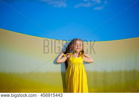 Ukrainian Girl 7 Years Old, She Is A Patriot Of Ukraine, Dressed In A Yellow Dress Against A Blue Sk