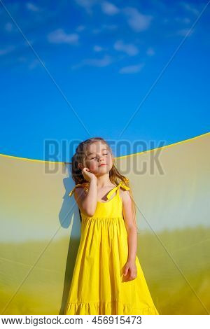 Ukrainian Girl 7 Years Old, She Is A Patriot Of Ukraine, Dressed In A Yellow Dress Against A Blue Sk