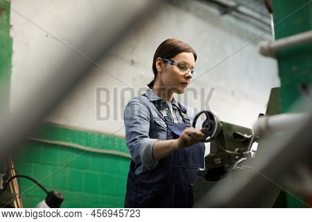 Serious Middle-aged Female Factory Worker In Protective Goggles Using Tailstock While Processing Det