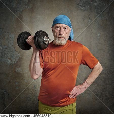 Casual Portrait Of Old Bearded  Man (in Late 60s) Exercising With Heavy Dumbbell, Active Senior And 