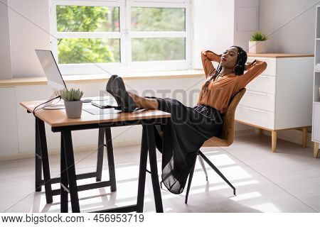 Side View Of Relaxed Young Businesswoman Sitting Feet Up At Office Desk