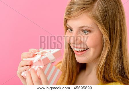 ピンクの背景に分離されたギフトを開く大喜びの女の子
