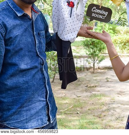 Indian Couple Posing For Maternity Baby Shoot. The Couple Is Posing In A Lawn With Green Grass And T