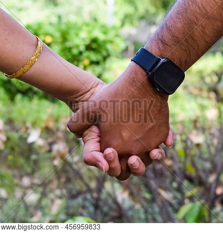Indian Couple Posing For Maternity Baby Shoot. The Couple Is Posing In A Lawn With Green Grass And T