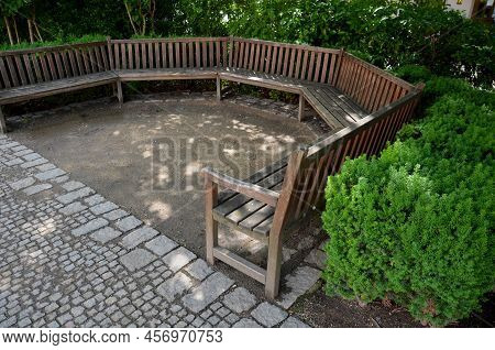 Arch Of The Flowerbed Surround The Wooden Bench In The Park. The Bench Is Bent Like A Horseshoe, Wit