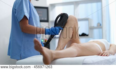 Doctor Hands In Blue Medical Gloves Hold Depilatory Machine And Use It On Woman Legs. Laser Hair Rem