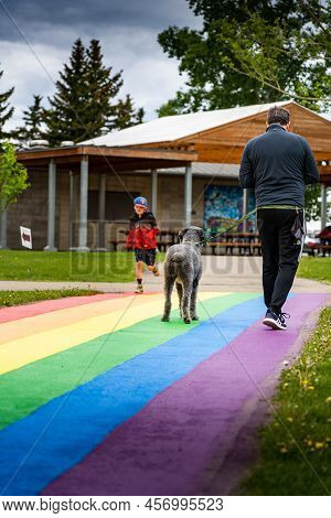 Airdrie Alberta Canada, June 12 2022: A Man And His Dog Walk Along A Path Painted In Rainbow Stripes