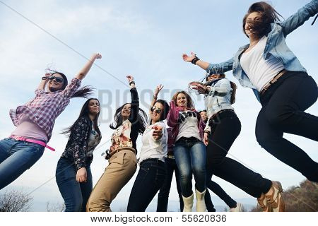 Happy teen girls having good fun time outdoors jumping on green meadow