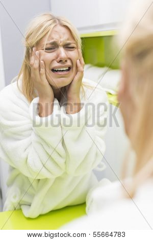 Young ill woman crying while looking at mirror in bathroom