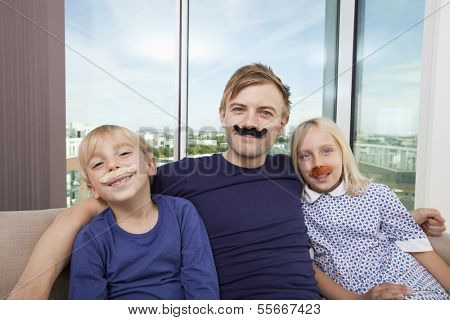 Portrait of happy father and children with artificial mustache sitting on sofa at home