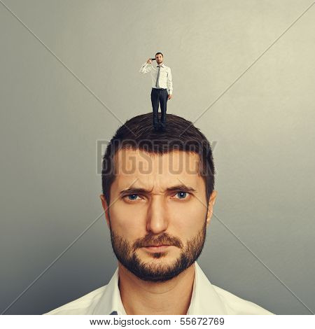 sullen man with small man on the head over grey background