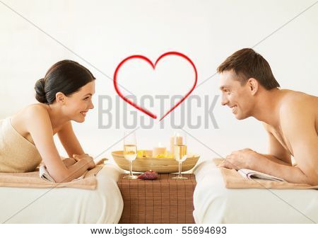 spa, beauty, love and happiness concept - smiling couple with candles in spa salon drinking champagne