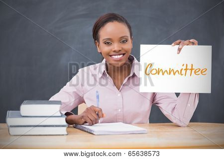 Happy teacher holding page showing committee in her classroom at school