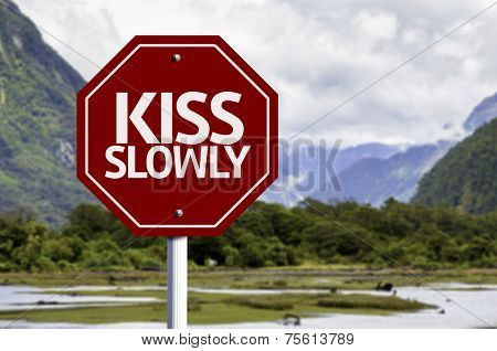 Kiss Slowly red sign with a landscape background