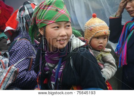Hmong woman carrying child and wearing traditional attire.