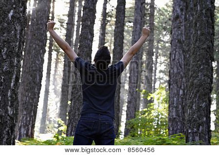 Man firar med armar lyfte i skogen