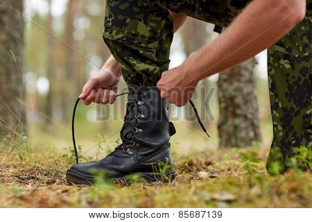 war, hiking, army and people concept - close up of soldier boots and hands tying bootlaces in forest