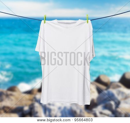 Close Up Of A White T-shirt On The Rope. Sea And Rocks In A Blur As A Background.