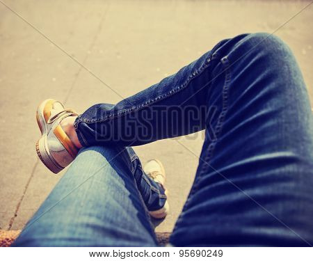 a hipster sitting downtown with crossed legs on a sidewalk bench on a sunny day toned with a retro vintage instagram filter app or action