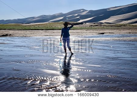 Woman silhouette in shallow river by great sand dunes. Great Sand Dunes National Park and Preserve. Denver. San Luis Valley. Alamosa Saguache County Colorado. United States.