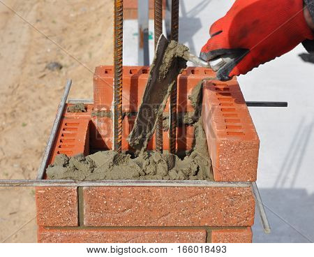 Bricklaying closeup. Bricklayer hand holding a putty knife and building a brick fence column with iron bar.