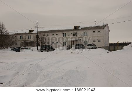 Old two-storied  house in winter with snow, cars and trees on the yard. Poverty and misery, North