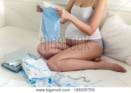 young pregnant girl in bed with baby stuff and keep the suit