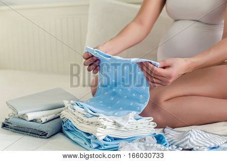 young pregnant girl in bed with baby stuff and keep the suit