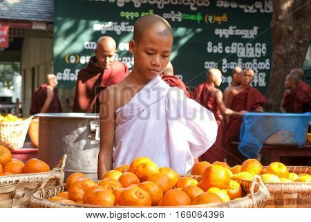 Mandalay Myanmar 17 January 2010: Young monk in the kitchen in front of a pile of oranges at Mahagandayon Monastery on Mandalay Myanmar