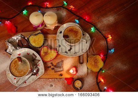 Two beautiful cups of cappuccino coffee with candles and chocolate for lovers in romantic atmosphere