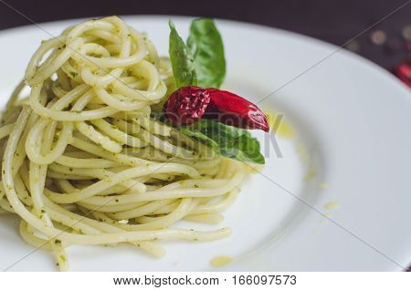 Close up italian pasta spaghetti with homemade green pesto sauce chili pepper and basil leaf. Delicious healthy vegetarian food. Italian food concept. Selective focus.