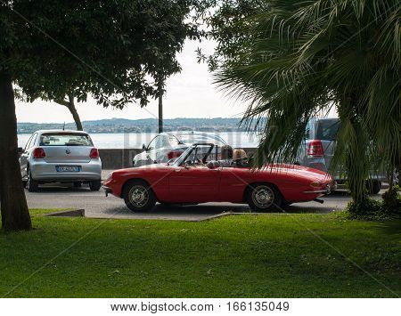 SIRMIONE, ITALY - MAY 5, 2016: Couple in vintage red cabriolet Alfa Romeo Giulietta Spider in Sirmione Garda Lake Italy