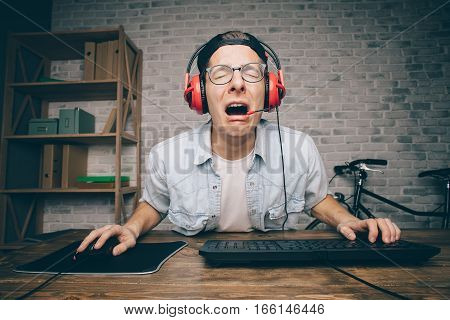Young man in red headphones and white shirt playing game at home and streaming playthrough or walkthrough video. Poor guy is crying because of fail. His ace expression is amazing and gorgeous.