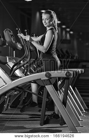 Young woman at the gym exercising. Run on on a machine. Jogging workout in dark fitness club. Cardio. Black and white.