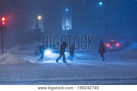 People cross road at heavy night winter snowstorm. Low visibility, street traffic. Very cold snowy weather.