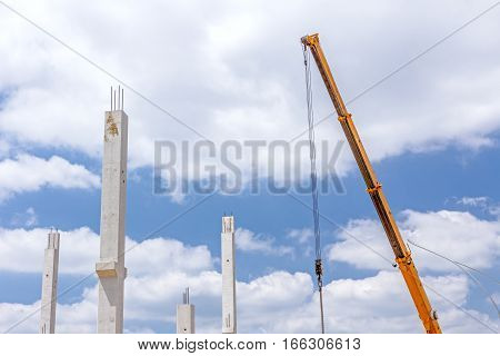 Crane arm is operating to assembly concrete pillars on new edifice.