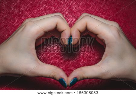 Women palms in the shape of a heart on a red background tekstured. Symbol of love Valentine Day, fourteen february.