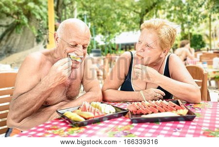 Senior couple having fun eating seasonal fruit in thai restaurant bar outdoors - Mature man and woman on active elderly vacation - Happy retirement concept with people together - Warm shadow filter