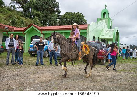 May 22, 2016 Florencia Costa Rica: local tico farmer woman riding her horse holding a toddler on lap celebrating harvest day