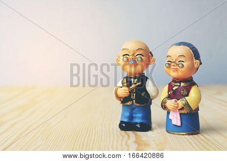 Grandma And Grandpa Dolls In Chinese Uniform Style Standing On Wooden Background. In Chinese New Yea