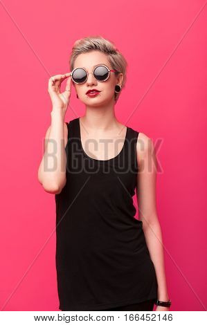 Fashion blond girl in black clothes with short hair and bright make-up on pink color background
