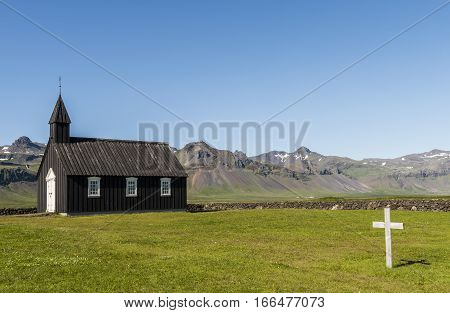 Black wooden Budakirkja at Saefellsnes with cementery and cross on Iceland.
