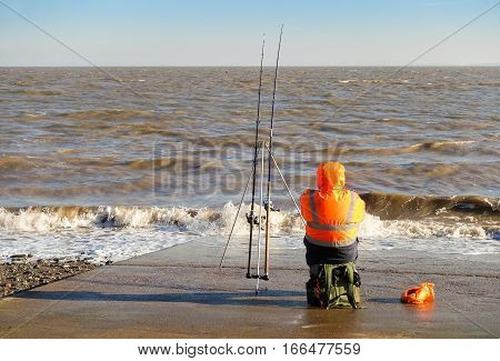 Penarth Vale of Glamorgan United Kingdom - January 22 2017: Angler fisherman sitting on the slipway in Penarth (near Cardiff) in winter fishing in the sea.