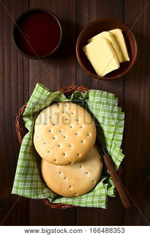 Traditional Chilean Hallulla bread rolls in basket with butter and strawberry jam above photographed overhead on dark wood with natural light
