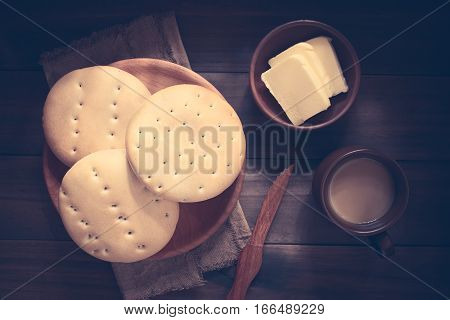 Traditional Chilean Hallulla bread rolls on wooden plate with butter and coffee with milk on the side photographed overhead on dark wood with natural light (Digitally Altered: Toned Image)